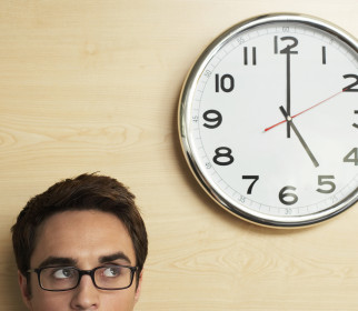 Young businessman wearing spectacles looking at clock on wooden